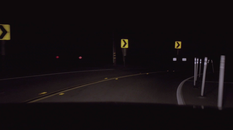 A dark road with signs warning of a sharp curve. (Screenshot: Twin Peaks)